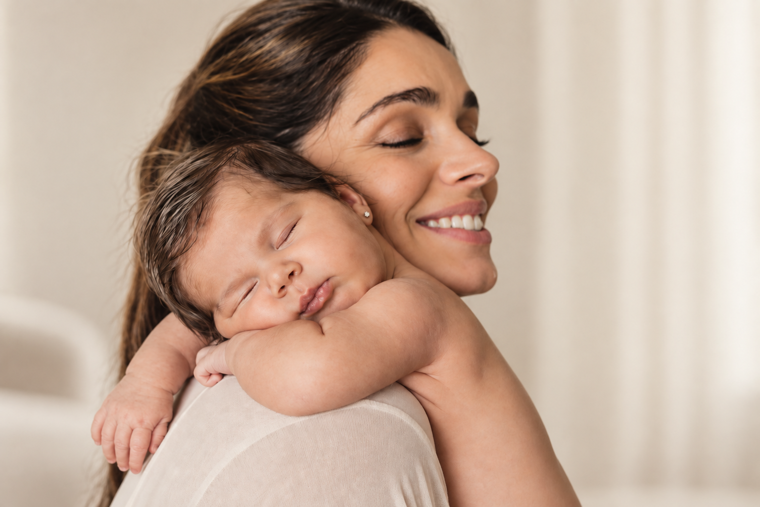 A smiling mother with her eyes closed cradling her sleeping newborn against her shoulder